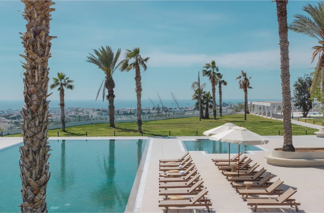 Piscine panoramique de Brown Paphos Hills entourée de palmiers avec vue sur la mer Méditerranée